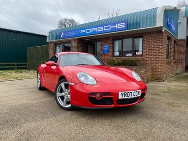 Red Porsche sports car parked outside a Porsche dealership.