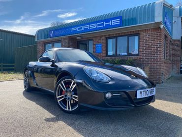 Black Porsche sports car parked outside a dealership on a sunny day.