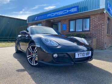 Black Porsche sports car parked outside a Porsche dealership on a sunny day.
