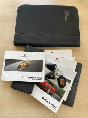 Porsche manuals, keys, and a Haynes service binder on a table.