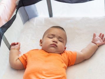 Baby peacefully sleeping on a soft surface, wearing an orange shirt.