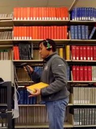 Worker scanning books on shelf.