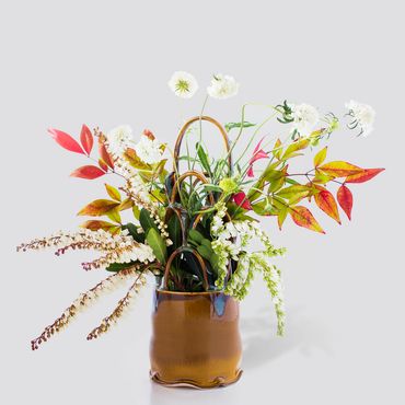 A vibrant autumnal flower arrangement in a brown vase.