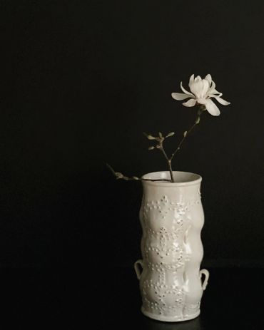 White flower in a decorative white vase against a dark background.