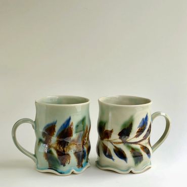 Two artistically designed ceramic mugs with leaf patterns.