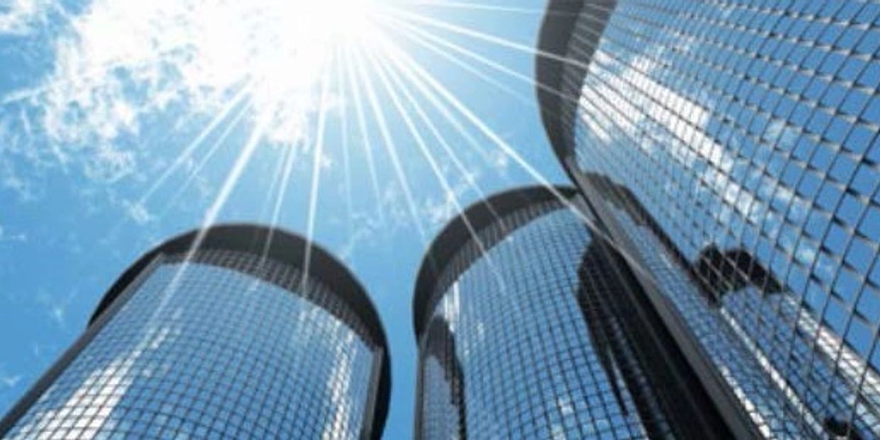 Sunlight gleams off three tall, cylindrical glass skyscrapers against a blue sky.