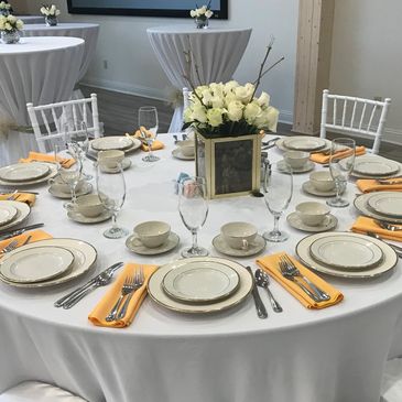 White linen on round table with china dinner plate, salad plate, cup, saucer, wine glass and silverware. White flower centerpiece gold napkins