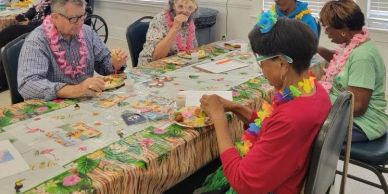 Seniors crafting at a decorated table, wearing leis.