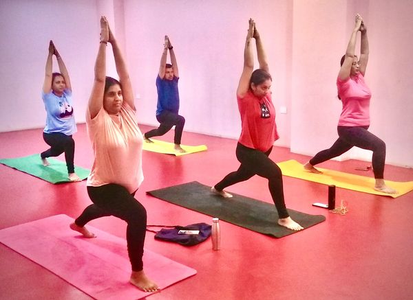 "A group of yoga students at Inner Axis Yoga Kulam practicing Virabhadrasana  in a bright studio
