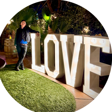 Person leaning against illuminated LOVE sign in garden at night.