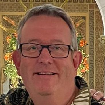 Smiling man with glasses in tropical setting.