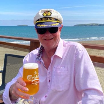 Man in captain hat holding a beer by the beach.