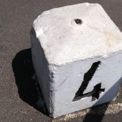 White concrete block with the number 4 painted in black on asphalt.