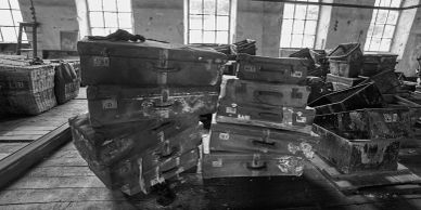 Old suitcases stacked in a warehouse with windows in the background.