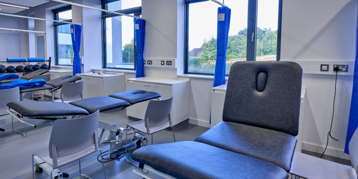 Physical therapy room with treatment tables and chairs.
