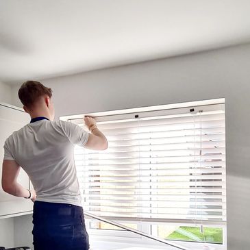Person adjusting white blinds on a window in a bright room.