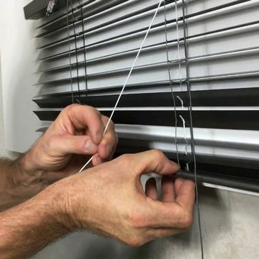 Hands repairing a broken blind cord on horizontal window blinds.