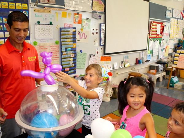 Man in red shirt making balloon animals for children in a colorful classroom.