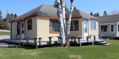 Cozy beige cottage with red trim on a green lawn near a birch tree.