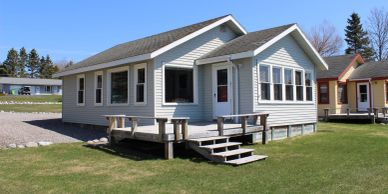 Small white house with a porch and steps on a grassy lawn.