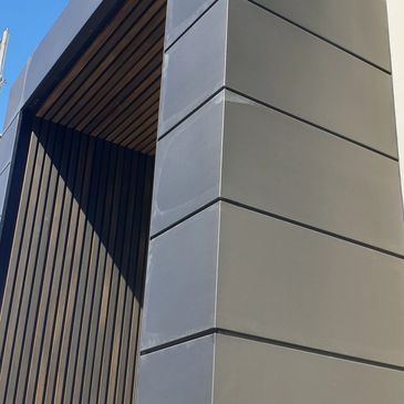 Modern building corner with grey panels and vertical wooden slats.