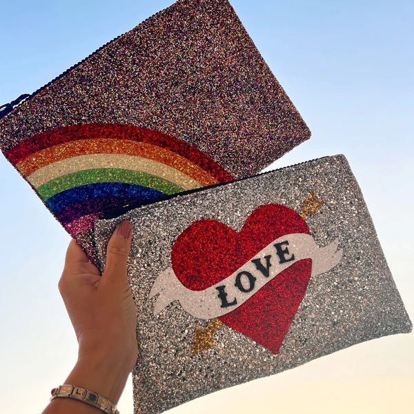 Love and rainbow glitter clutch bags held up to sky. 