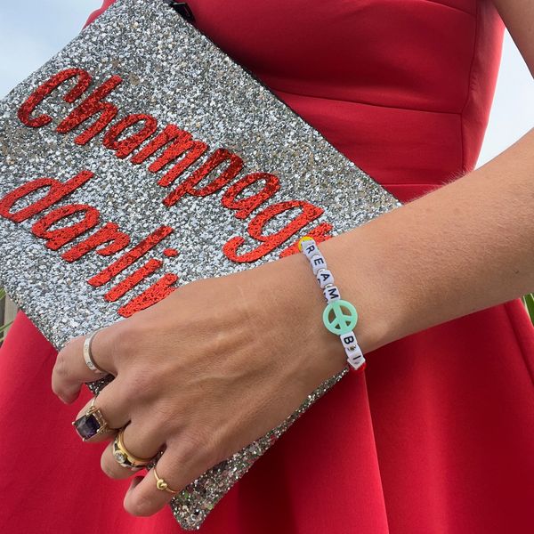 Champagne darling glitter clutch bag held by girl in red dress. 