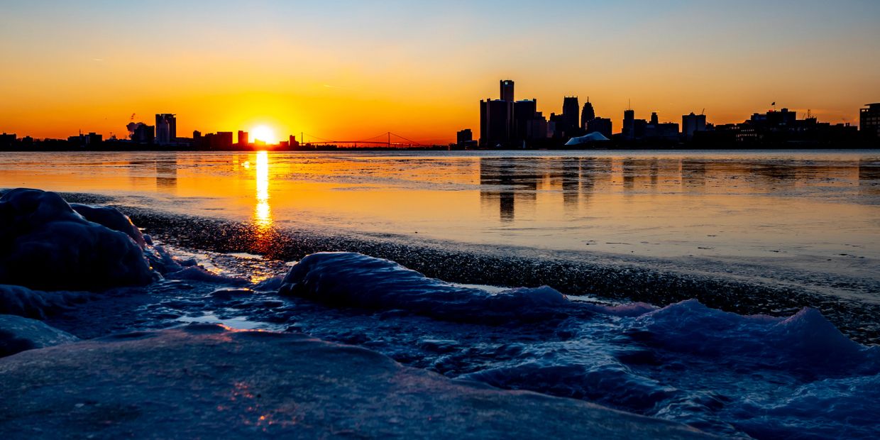 Sunset over a frozen river with a city skyline silhouette.