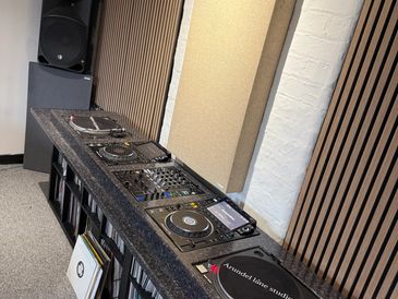 Professional DJ setup with turntables, mixer, and records in a sound-treated room.