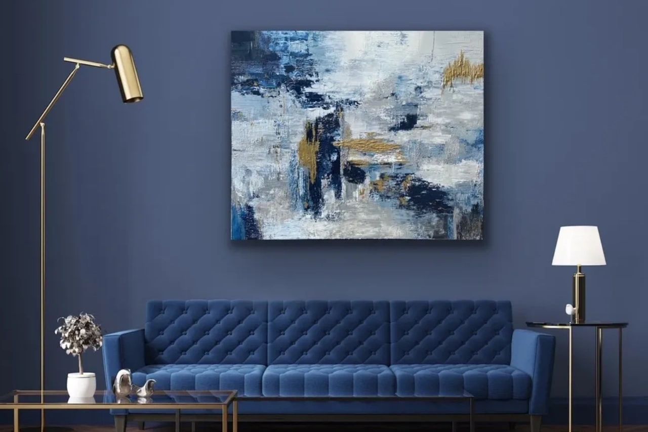 Navy, gold, white and grey abstract art hanging against a blue wall