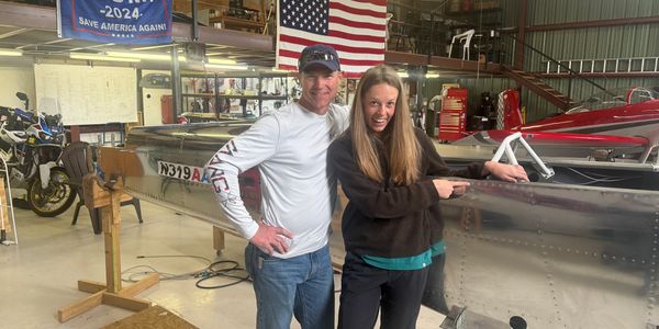 Two people smiling in a hangar near an aircraft.