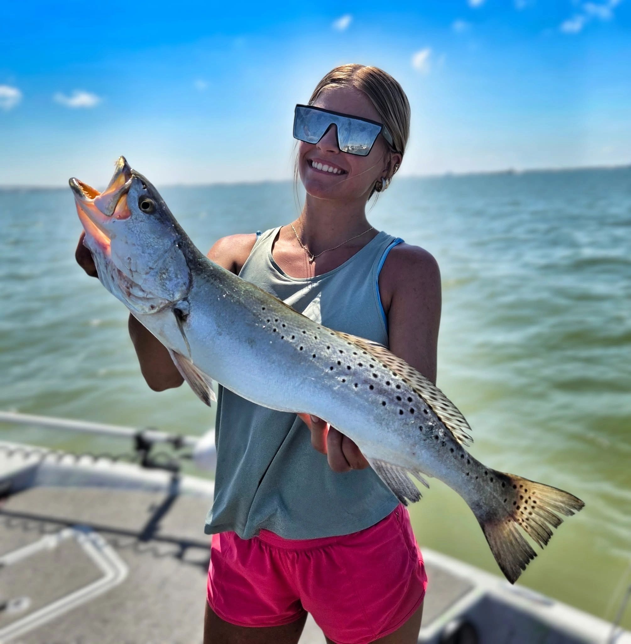 Smiling woman holding a large fish on a sunny day by the water.