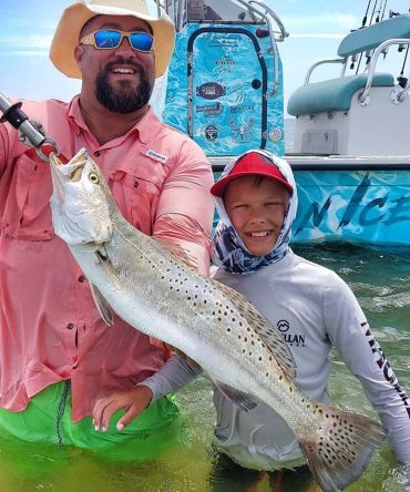 Man and boy proudly hold a large fish they caught by a boat.