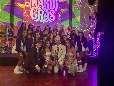 Group photo at a Mardi Gras celebration with colorful lights and festive attire.