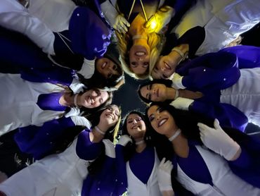 A group of smiling women in blue and white uniforms standing in a circle, looking down at the camera.