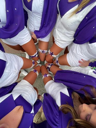 Group of women in purple and white outfits standing in a circle.