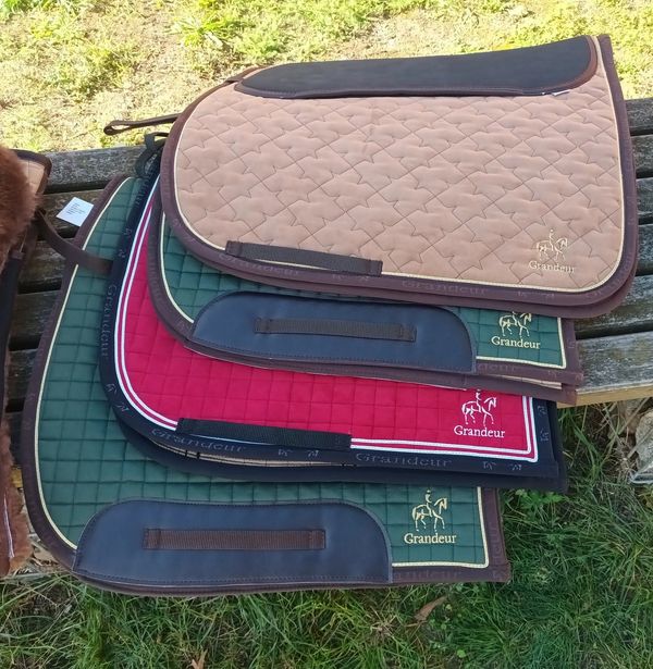 Stack of colorful Grandeur saddle pads on a bench.