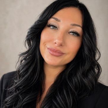 Woman with long black curly hair and a black outfit smiling.