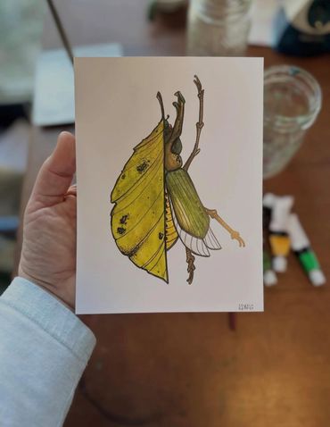 Hand holding artwork of a beetle with a leaf wing.