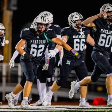 High school football players in black Matadors uniforms celebrating on the field.