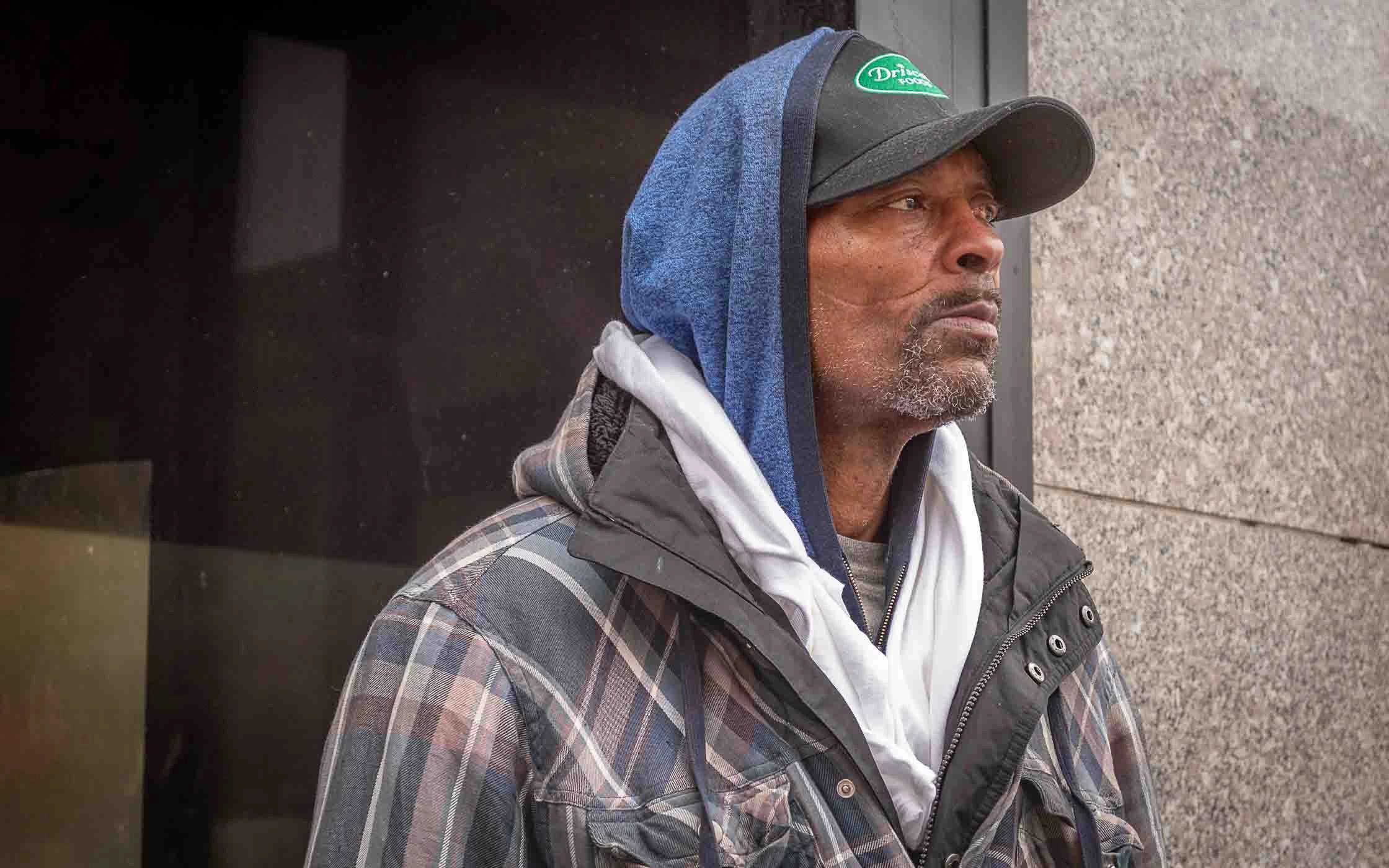 Man wearing a hat and layered jackets looks thoughtfully sideways.