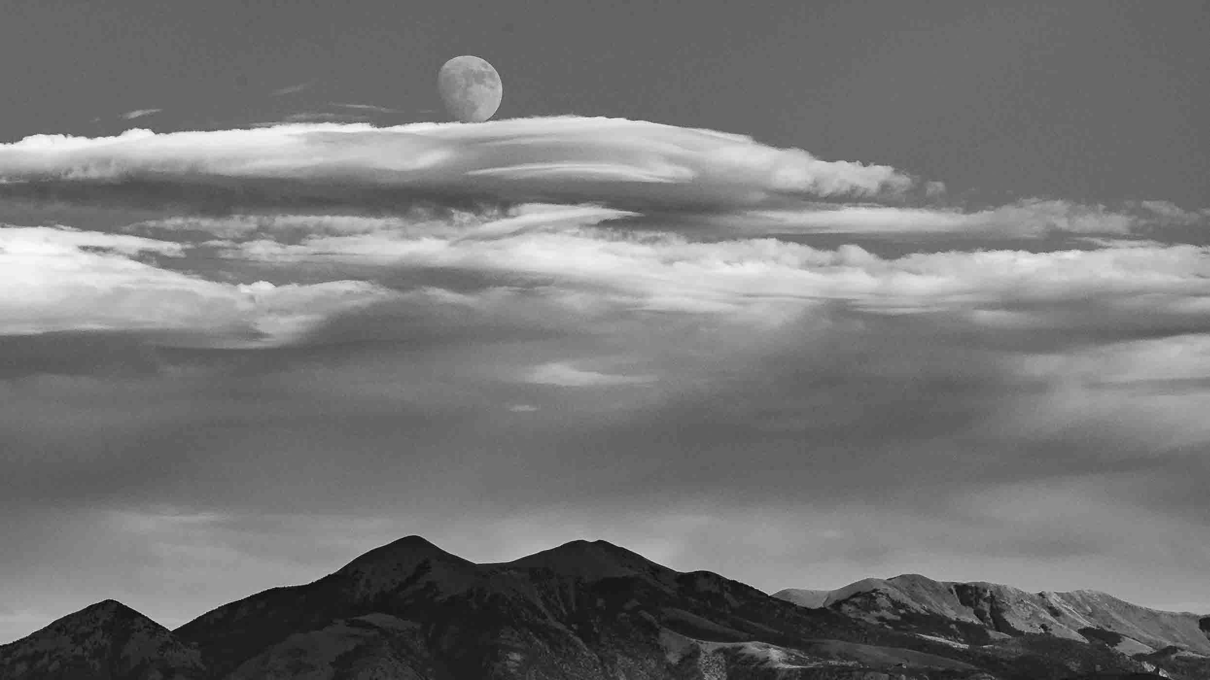 Moon rising above mountains with clouds in black and white.
