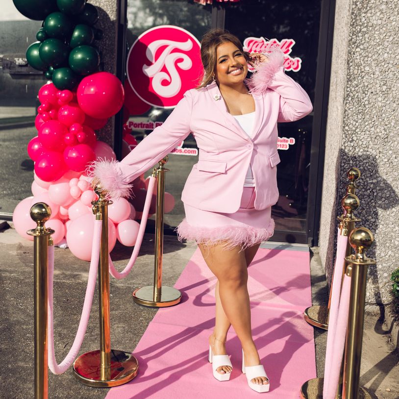 Woman in pink outfit posing on pink carpet outside.