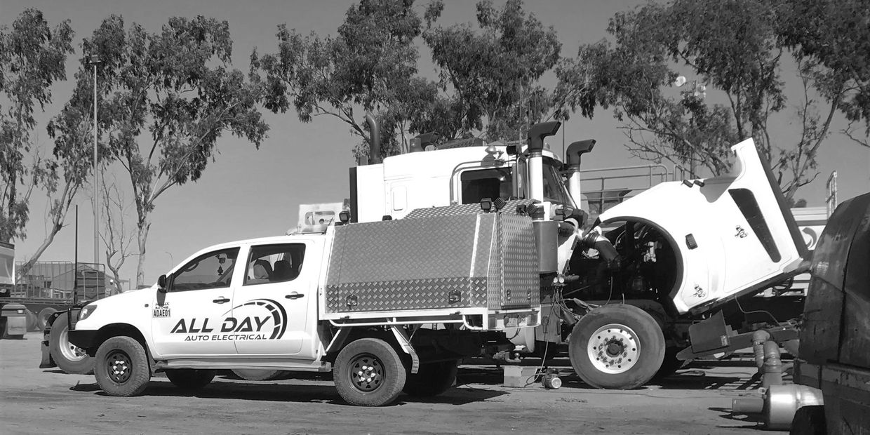 Service truck and a truck with lifted hood in an outdoor workspace.