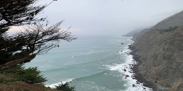 A rocky coastline with waves crashing under a cloudy sky.