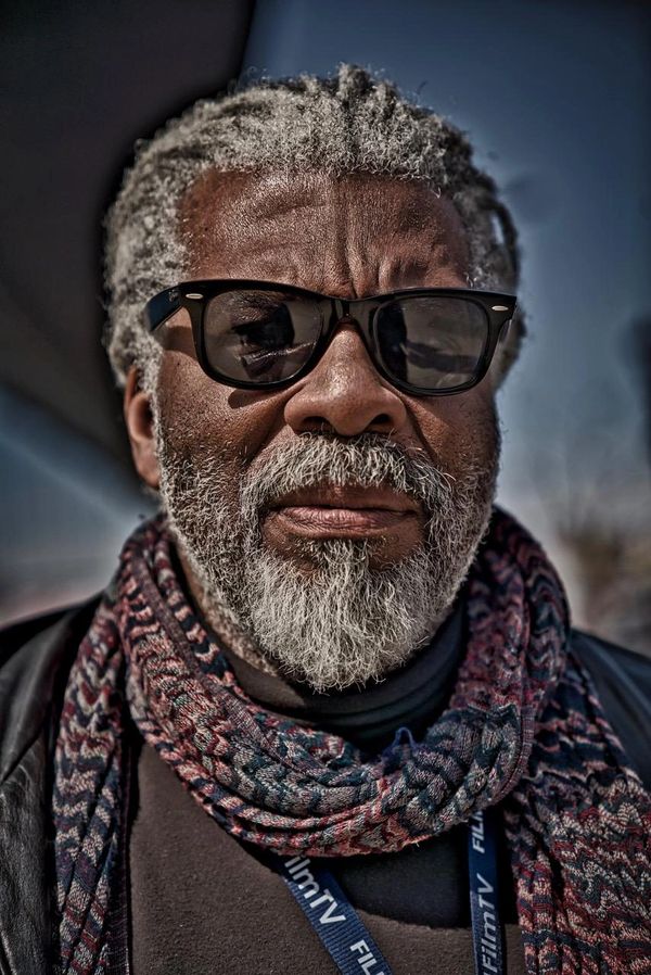 Portrait of a bearded man wearing sunglasses and a patterned scarf.