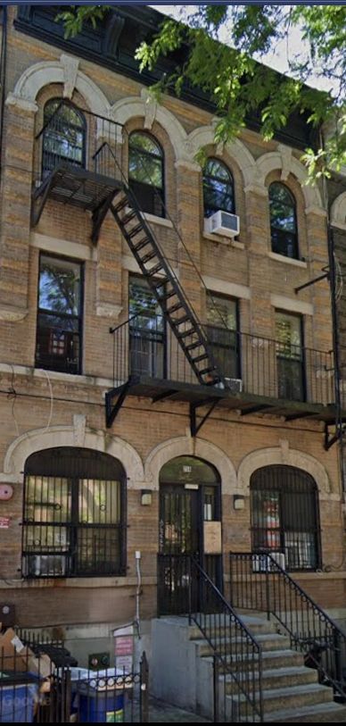 Three-story brick building with fire escape and barred windows.