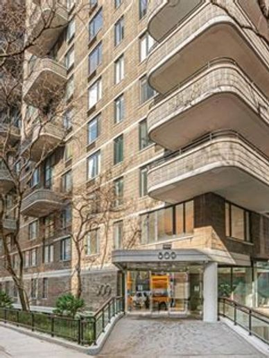 Entrance of a residential apartment building with balconies and trees.
