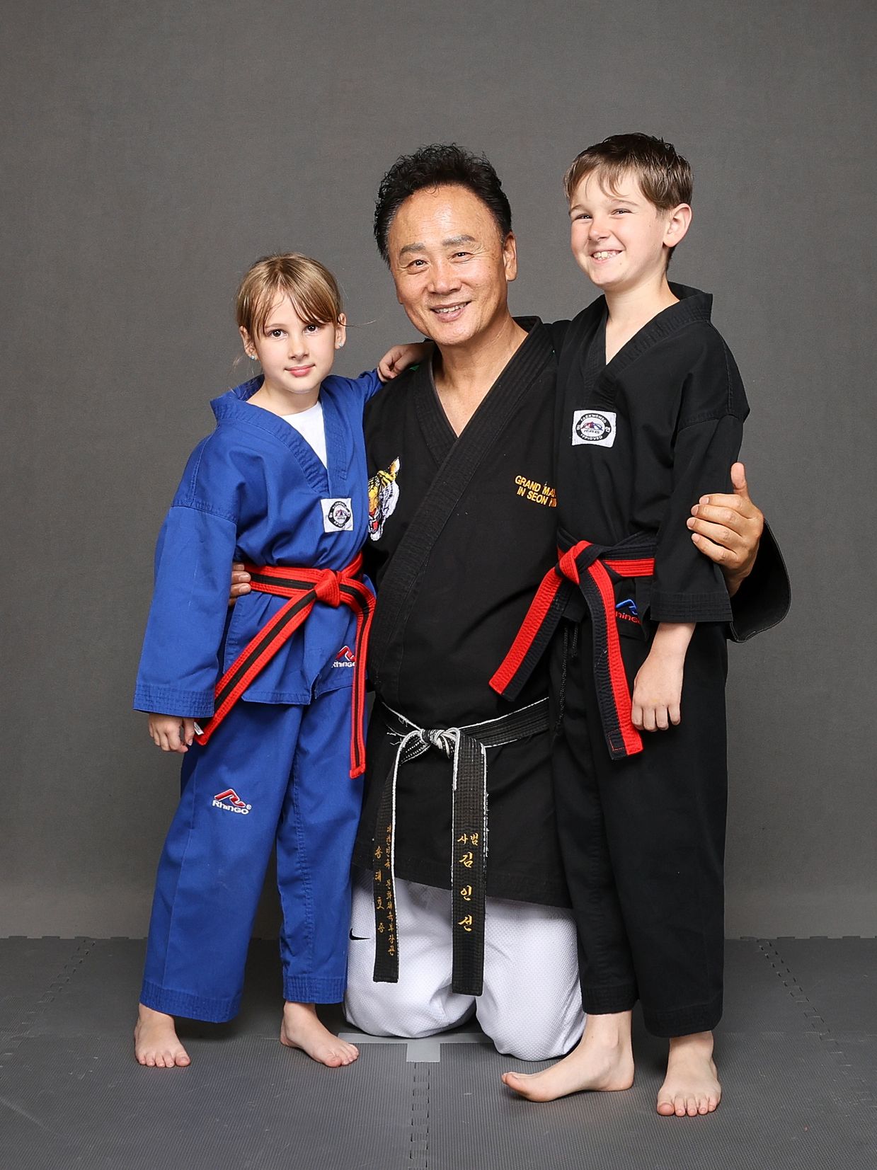Martial arts instructor posing with two children in uniforms.