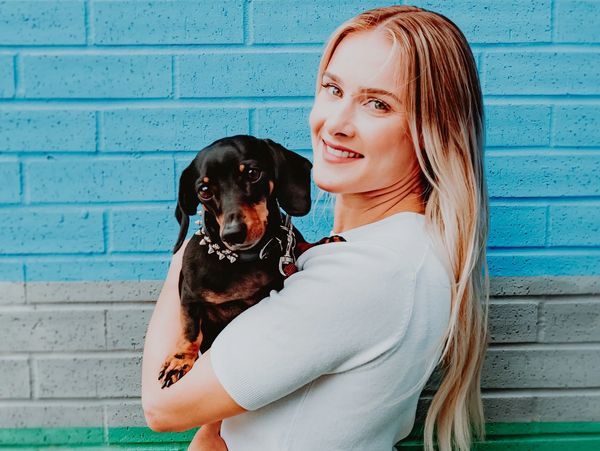 Woman with blonde hair smiling whilst holding black and brown sausage dog.